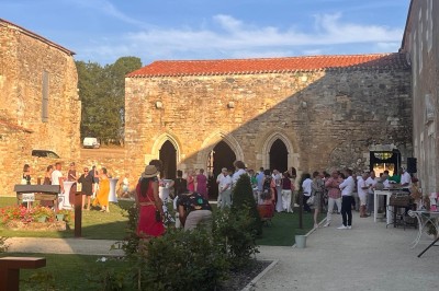 Cour intérieure d'un bâtiment historique en pierre, aménagée avec des tables hautes et éclairée par un soleil éclatant.