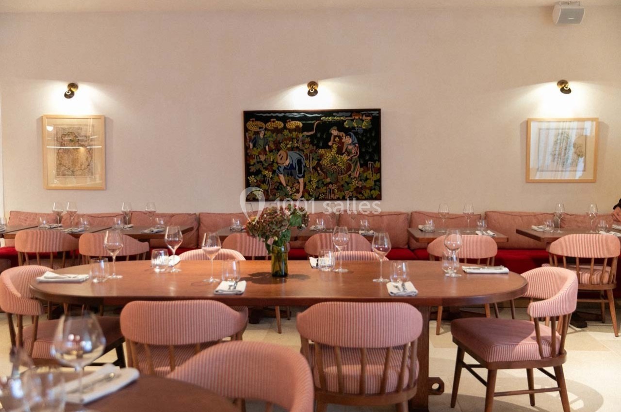 Salle de restaurant lumineuse avec tables en bois, chaises roses, banquettes rouges et œuvres d'art accrochées aux murs.