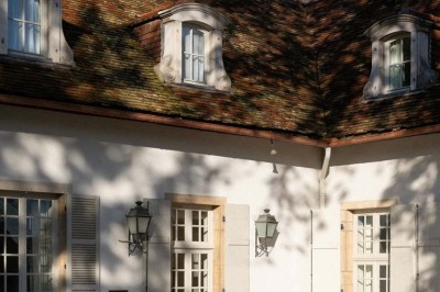 Chambre lumineuse sous combles avec poutres apparentes, lit à baldaquin, table en bois et fenêtre donnant sur l'extérieur.