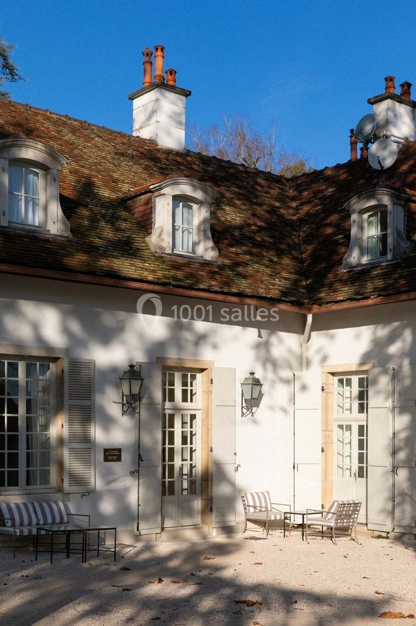 Façade d'une maison avec toit en tuiles, fenêtres mansardées et terrasse aménagée sous un ciel bleu.