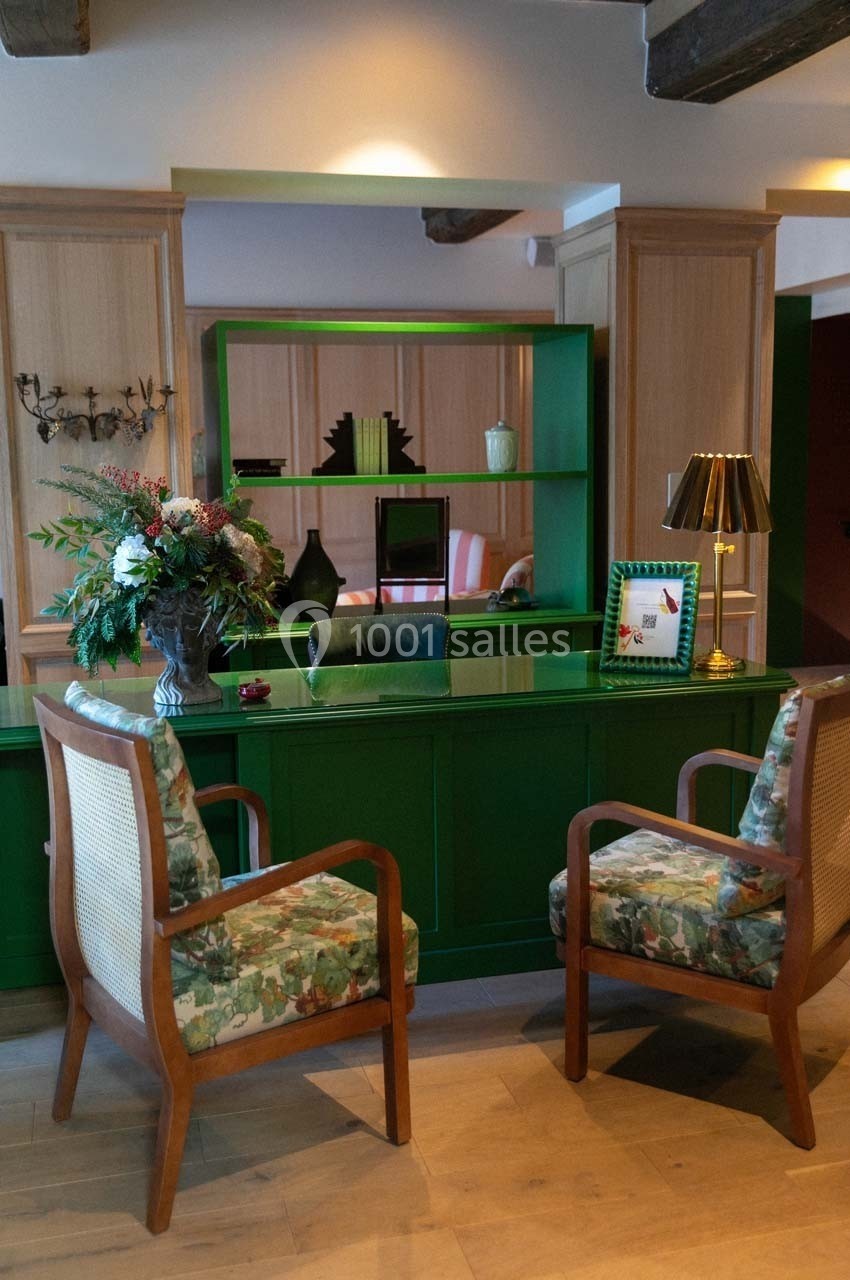 Bureau avec comptoir vert, deux fauteuils en bois, étagères décorées et bouquet de fleurs dans un intérieur chaleureux.