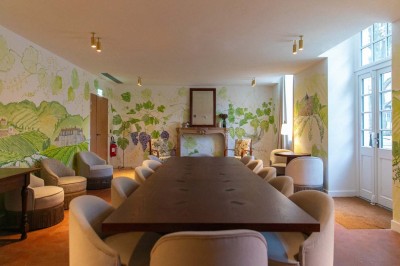 Salle de réunion lumineuse avec une grande table en bois, des fauteuils blancs et des fresques murales représentant des…