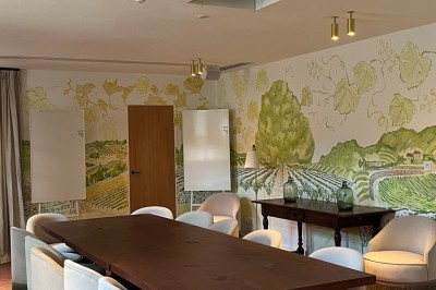 Salle de réunion lumineuse avec une grande table en bois, des fauteuils blancs et des fresques murales représentant des…