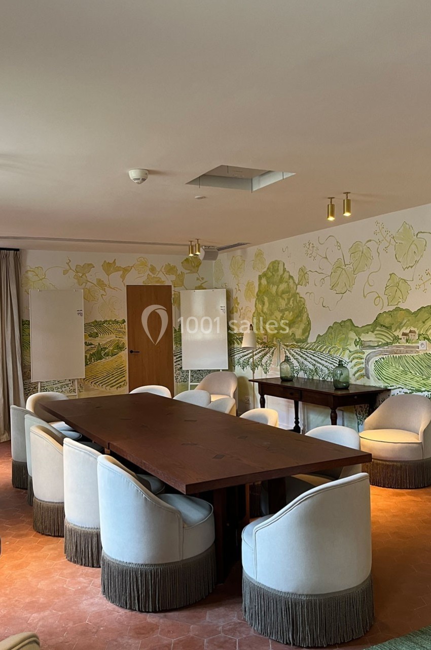 Salle de réunion lumineuse avec une grande table en bois, des fauteuils blancs et des fresques murales représentant des…