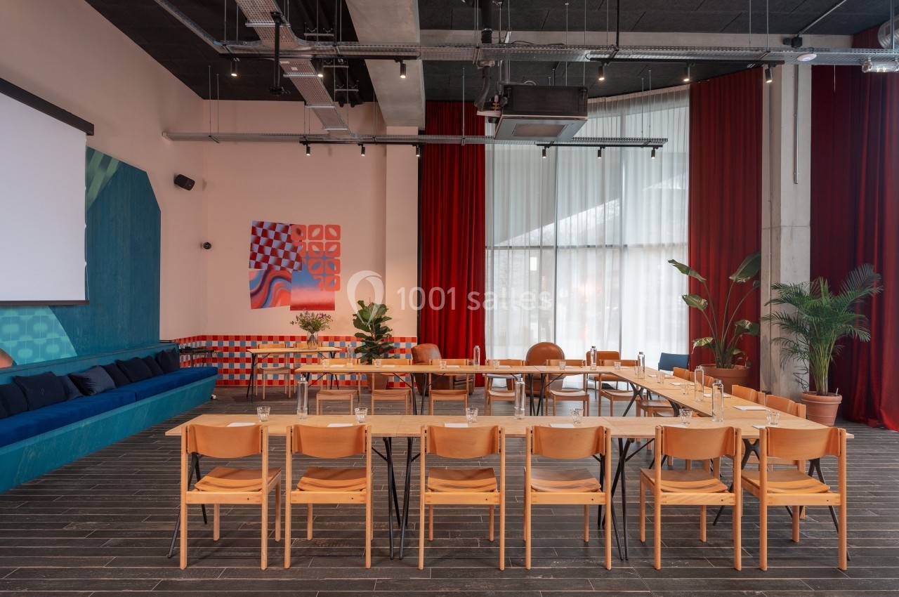 Salle de réunion moderne avec chaises en bois disposées autour de tables, décorée de plantes et d'œuvres murales colorées.