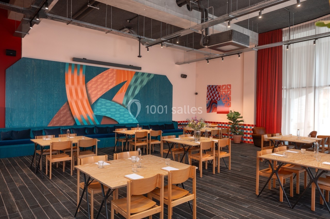 Salle de restaurant moderne avec tables en bois, chaises assorties et mur décoré d'une fresque colorée.