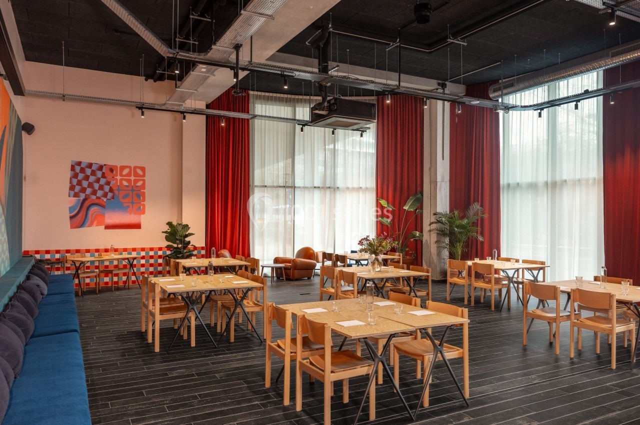 Salle de restaurant moderne avec tables en bois, chaises assorties, grandes fenêtres et décoration murale colorée.