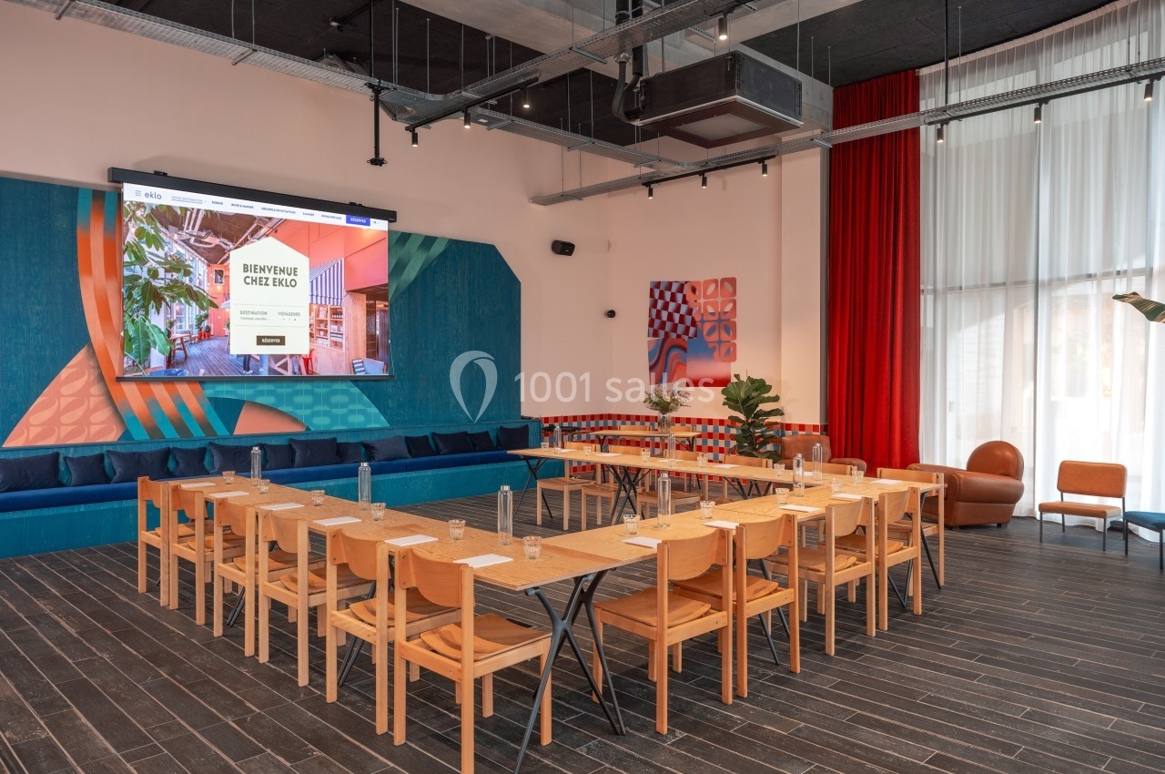 Salle de réunion moderne avec tables en bois disposées en U, écran de présentation et décorations colorées.