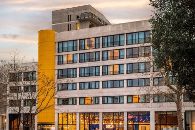Couloir d'hôtel avec murs roses, moquette bleue à motifs et portes numérotées de chaque côté.
