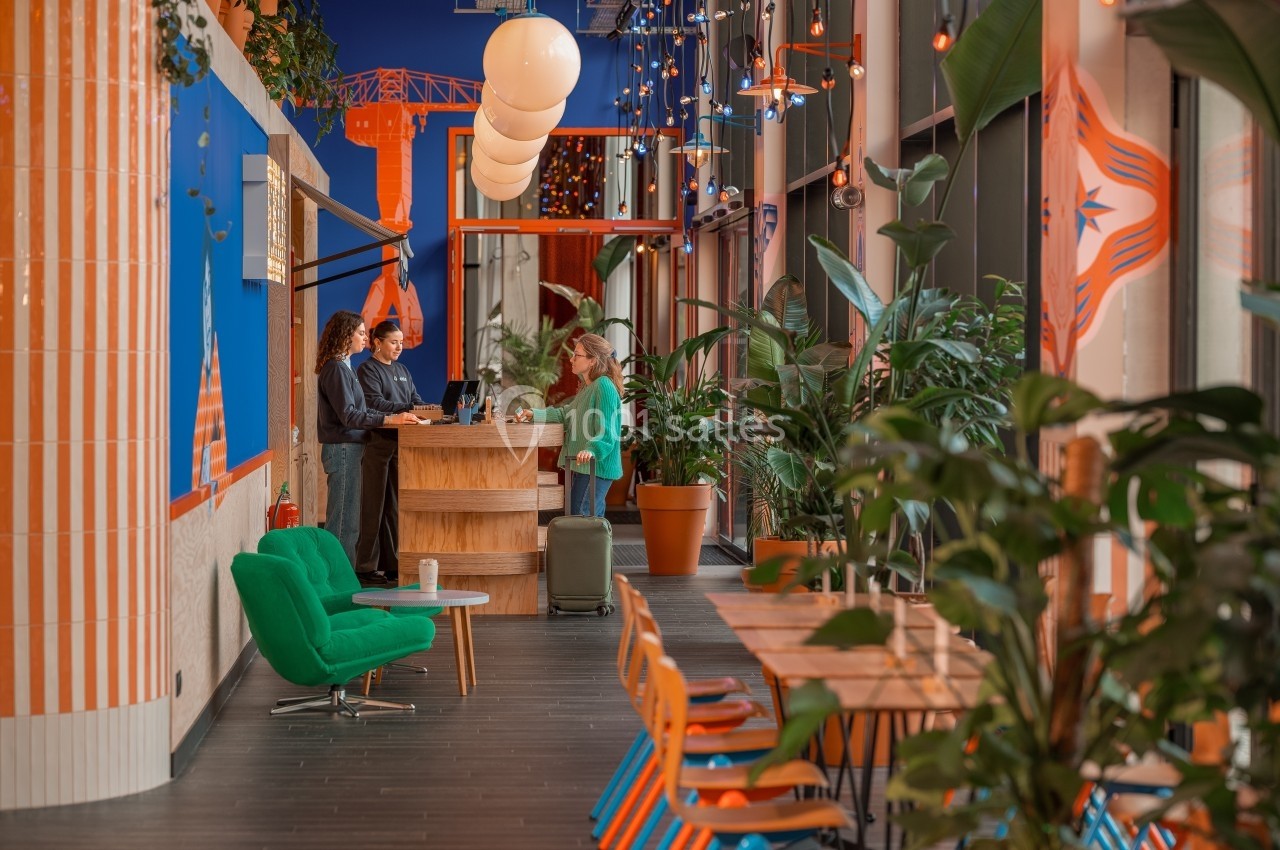 Espace de coworking coloré avec plantes, mobilier moderne, et personnes discutant près d'un comptoir en bois.