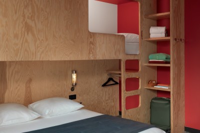 Couloir d'hôtel avec murs roses, moquette bleue à motifs et portes numérotées de chaque côté.