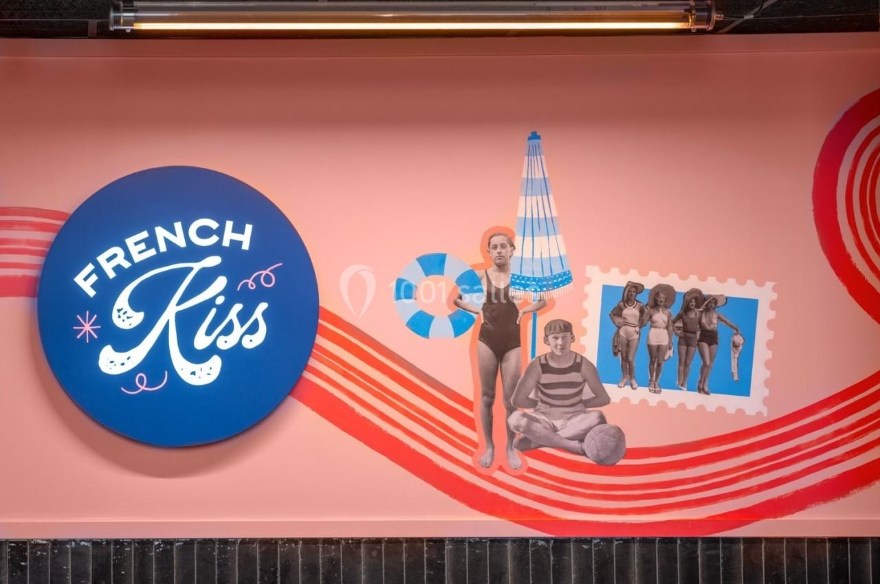 Fresque murale colorée avec des illustrations rétro de baigneurs et un panneau rond bleu marqué ’French Kiss’.