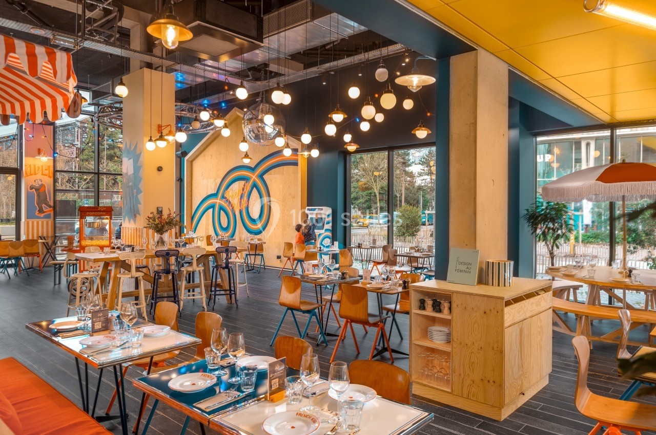 Salle de restaurant moderne et lumineuse avec des tables dressées, des luminaires suspendus et une décoration colorée.
