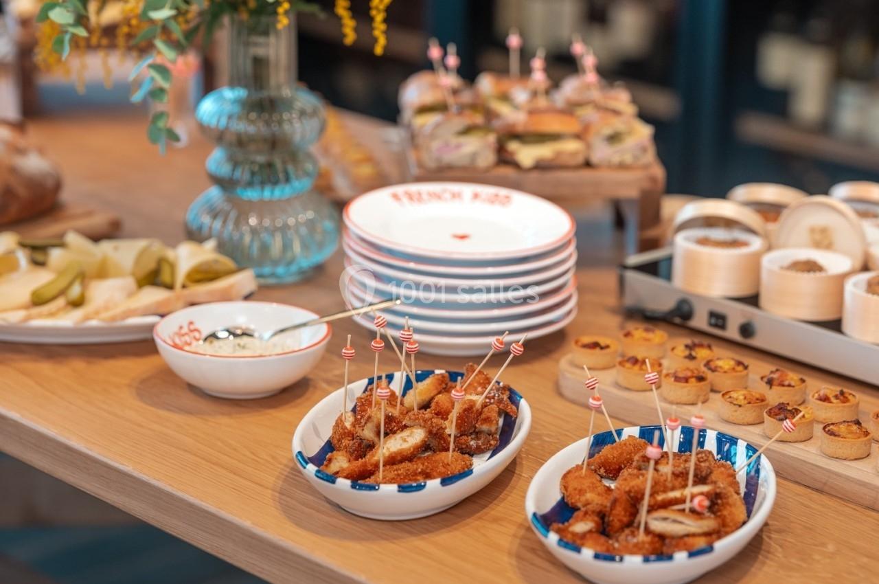 Assortiment de plats sur une table en bois, incluant bouchées apéritives, assiettes empilées et décor floral.