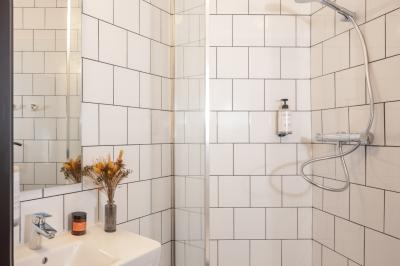 Douche avec carrelage blanc, robinetterie chromée, lavabo avec vase de fleurs séchées et savon.