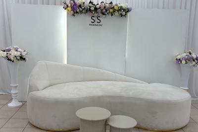 Salle de réception lumineuse avec tables rondes dressées, chaises blanches et décorations florales élégantes.