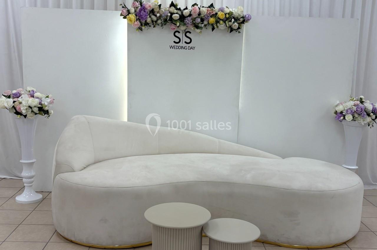 Canapé blanc incurvé devant un fond décoré de rideaux blancs, fleurs colorées et panneaux minimalistes.