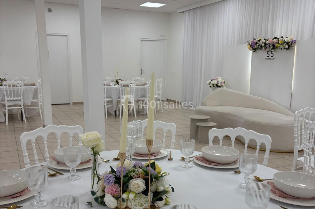 Salle de réception lumineuse avec tables dressées, décor floral et canapé blanc en arrière-plan.