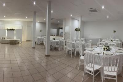 Salle de réception lumineuse avec tables rondes dressées, chaises blanches et décorations florales élégantes.