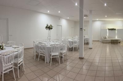 Salle de réception lumineuse avec tables rondes dressées, chaises blanches et décorations florales élégantes.