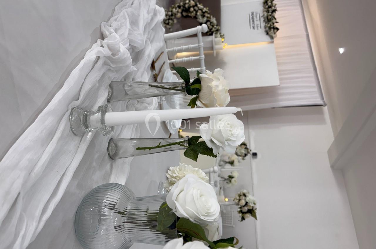 Bougies blanches et roses dans des vases en verre décorent une table recouverte d'une nappe blanche.