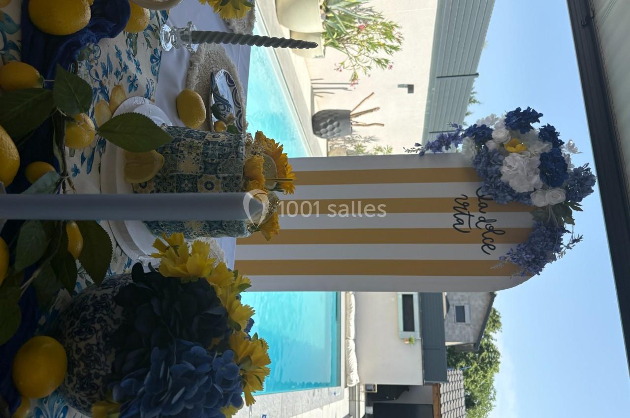 Décoration de table estivale avec fleurs bleues et jaunes, citrons et bougies, près d'une piscine en extérieur.