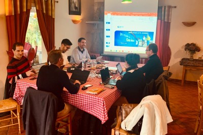 Plusieurs voitures blanches stationnées sur un parking en gravier, entouré de haies et de bâtiments.
