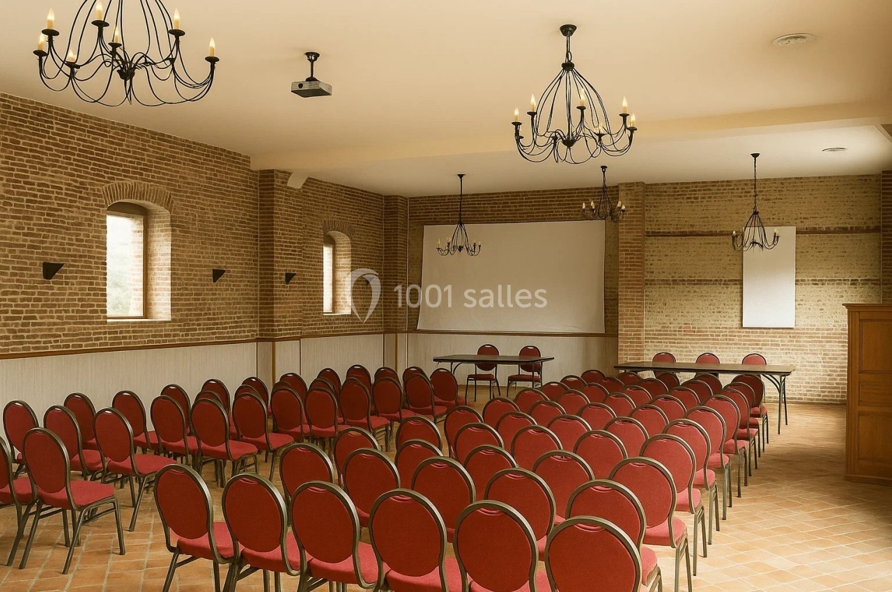 Salle de conférence avec des chaises rouges alignées, un écran blanc et des murs en briques apparentes.