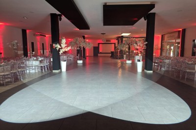 Salle de réception décorée avec des lumières rouges, tables dressées et projection lumineuse au sol.