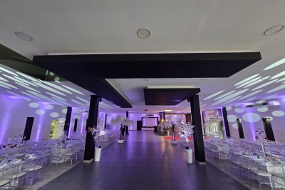 Salle de réception spacieuse avec éclairage rouge et blanc, tables décorées et chaises transparentes.