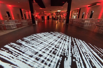 Salle de réception spacieuse avec éclairage rouge et blanc, tables décorées et chaises transparentes.