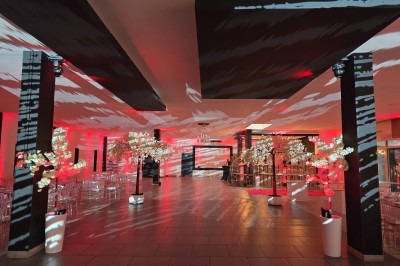 Salle de réception spacieuse avec éclairage rouge et blanc, tables décorées et chaises transparentes.