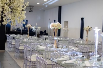 Salle de réception spacieuse avec éclairage rouge et blanc, tables décorées et chaises transparentes.