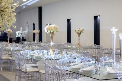 Salle de réception spacieuse avec éclairage rouge et blanc, tables décorées et chaises transparentes.