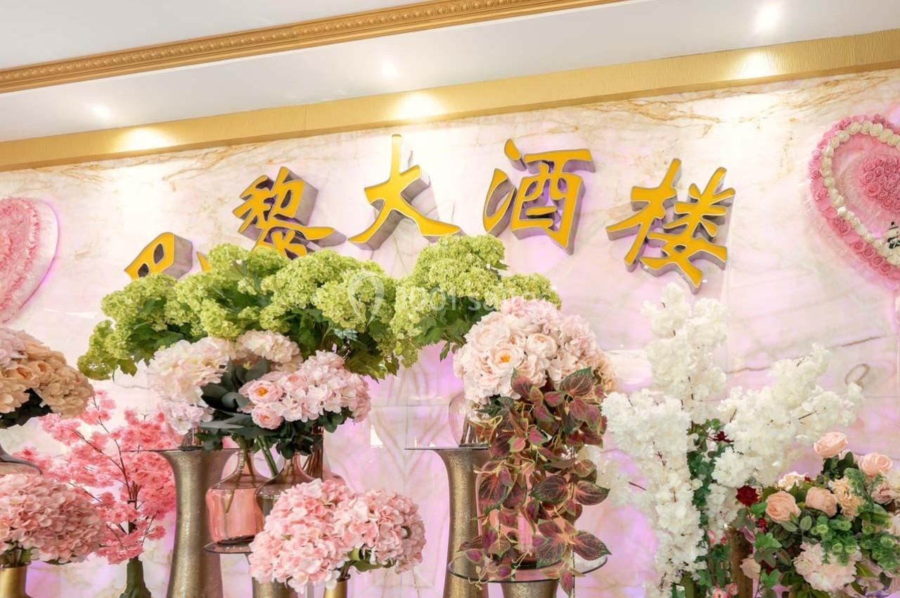 Arrangement floral coloré devant un mur décoratif avec des inscriptions dorées et un fond rose orné de motifs.