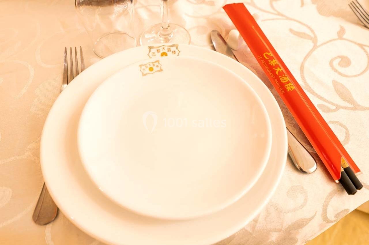 Assiette blanche avec des couverts, un verre et des baguettes rouges posées sur une nappe claire.
