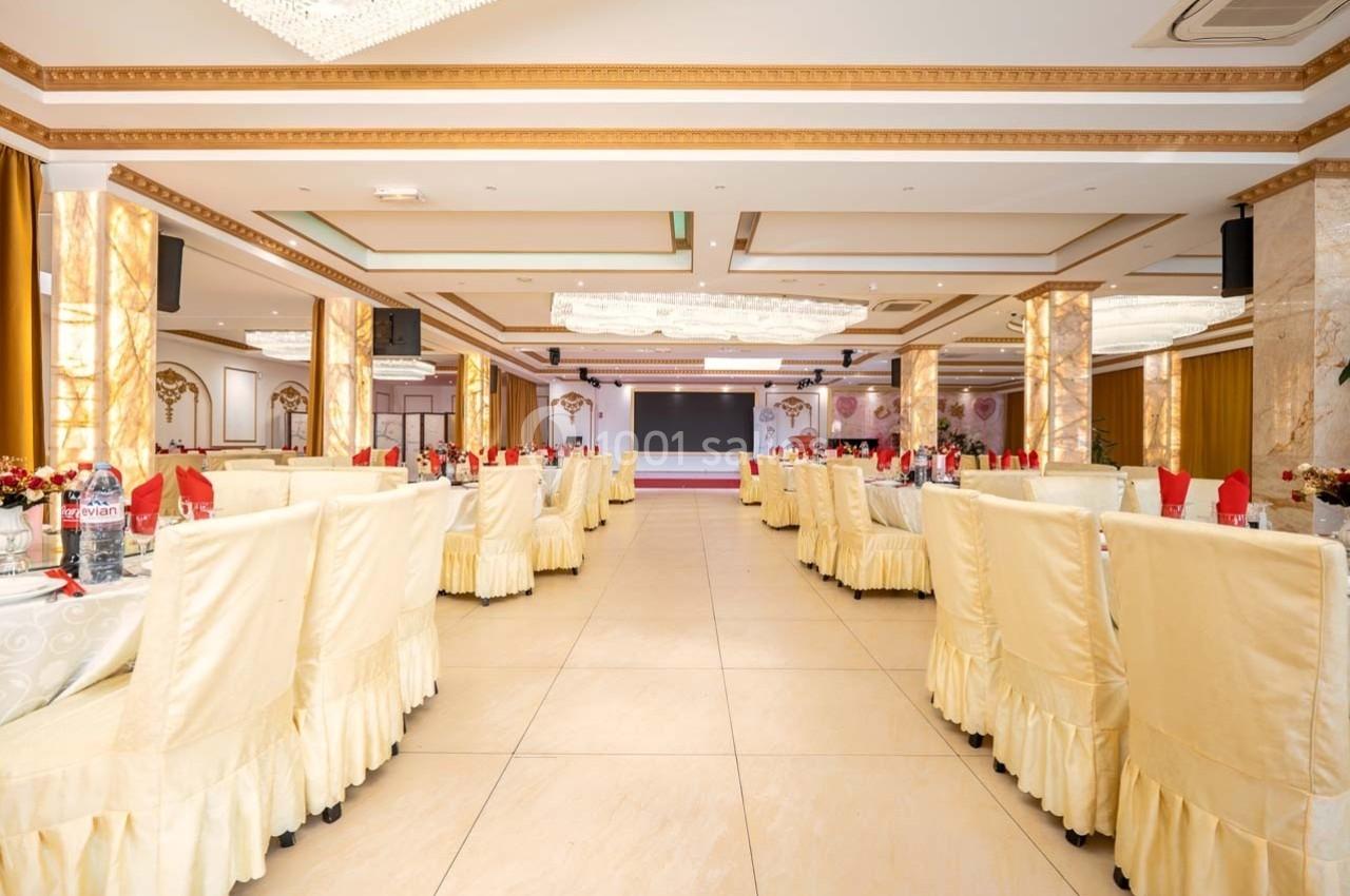 Salle de réception spacieuse avec tables alignées, nappes blanches, chaises couvertes et décorations élégantes.