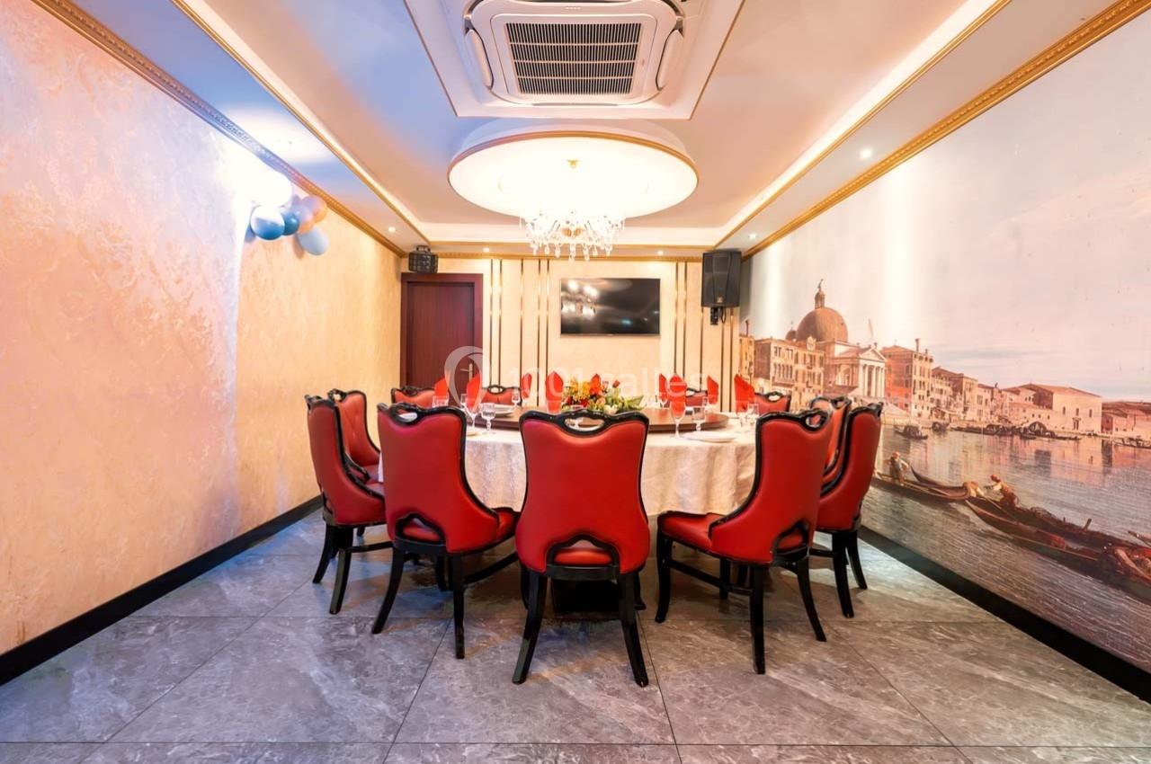Salle à manger élégante avec table ronde dressée, chaises rouges et fresque murale représentant un paysage urbain.