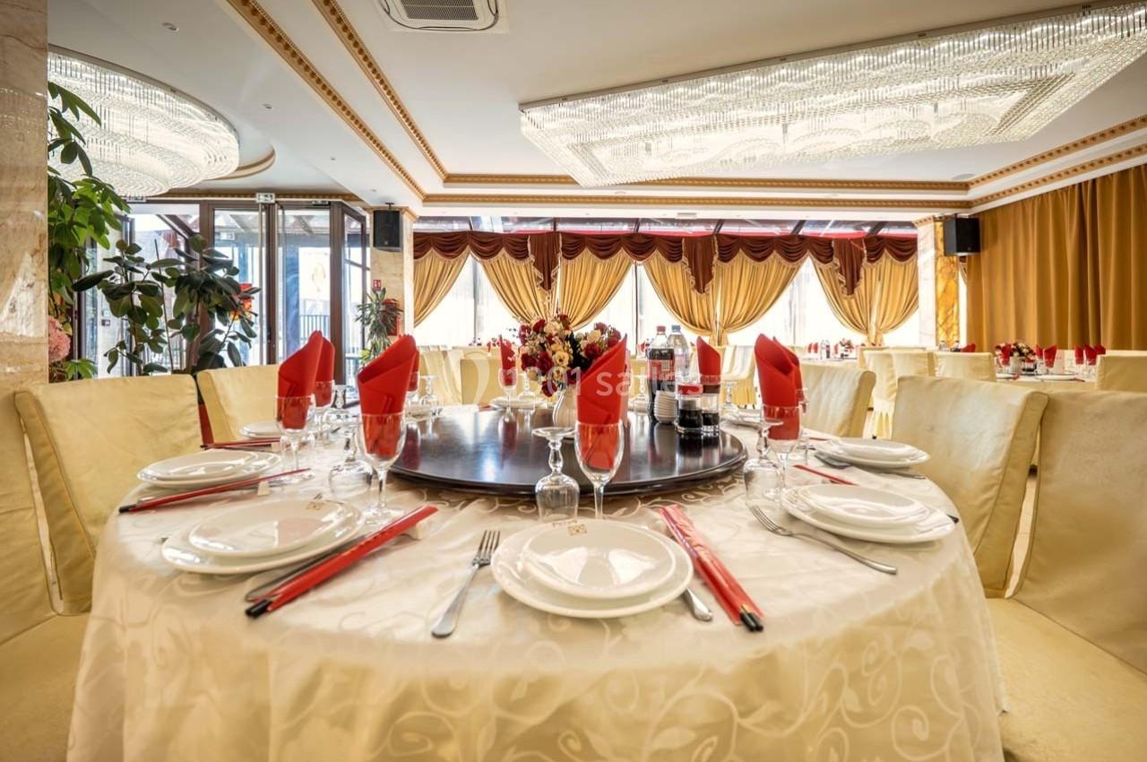Table dressée avec nappes blanches, serviettes rouges, vaisselle élégante et centre de table floral dans une salle lumineuse.