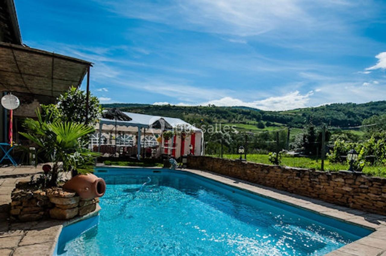 Piscine extérieure entourée de pierres, avec vue sur des collines verdoyantes sous un ciel bleu dégagé.