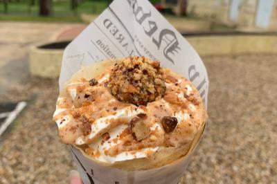 Crêpe garnie de crème fouettée, sauce caramel, éclats de noisettes et boule de praliné, tenue dans une main.