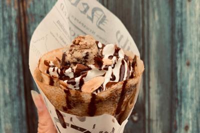 Crêpe garnie de crème fouettée, sauce caramel, éclats de noisettes et boule de praliné, tenue dans une main.