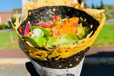 Crêpe garnie de crème fouettée, sauce caramel, éclats de noisettes et boule de praliné, tenue dans une main.