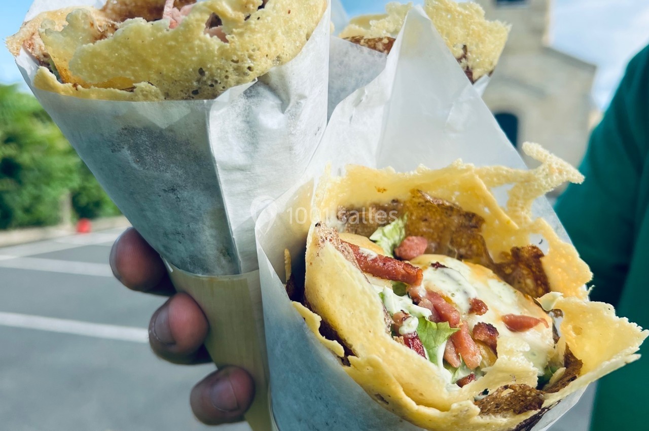 Deux cônes de crêpes garnies de légumes et de fromage, tenus à la main en extérieur par une journée ensoleillée.