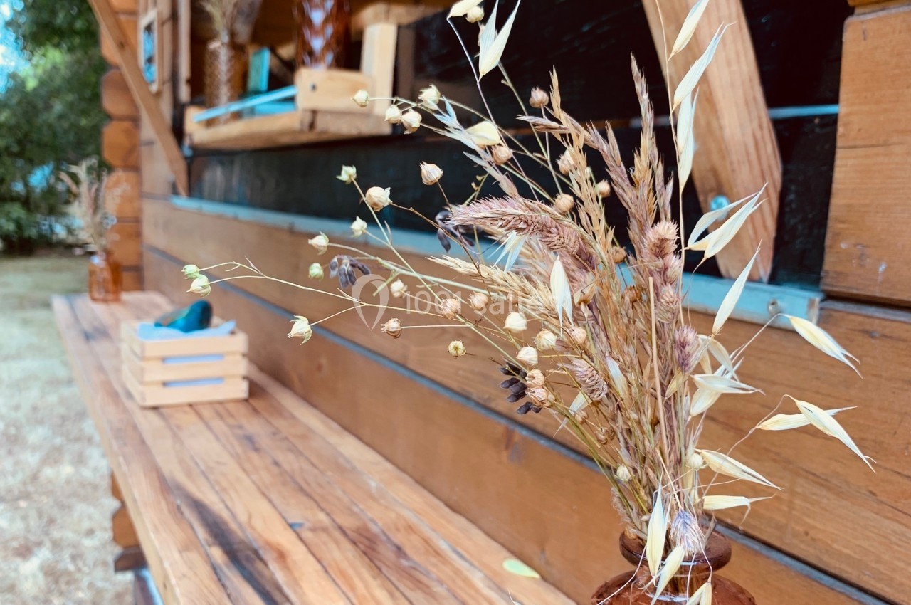 Vases en osier contenant des fleurs séchées disposés sur une terrasse en bois devant une structure en bois.