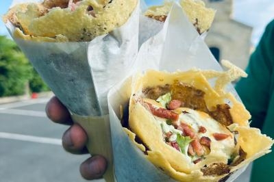 Crêpe garnie de crème fouettée, sauce caramel, éclats de noisettes et boule de praliné, tenue dans une main.