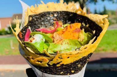 Crêpe garnie de crème fouettée, sauce caramel, éclats de noisettes et boule de praliné, tenue dans une main.