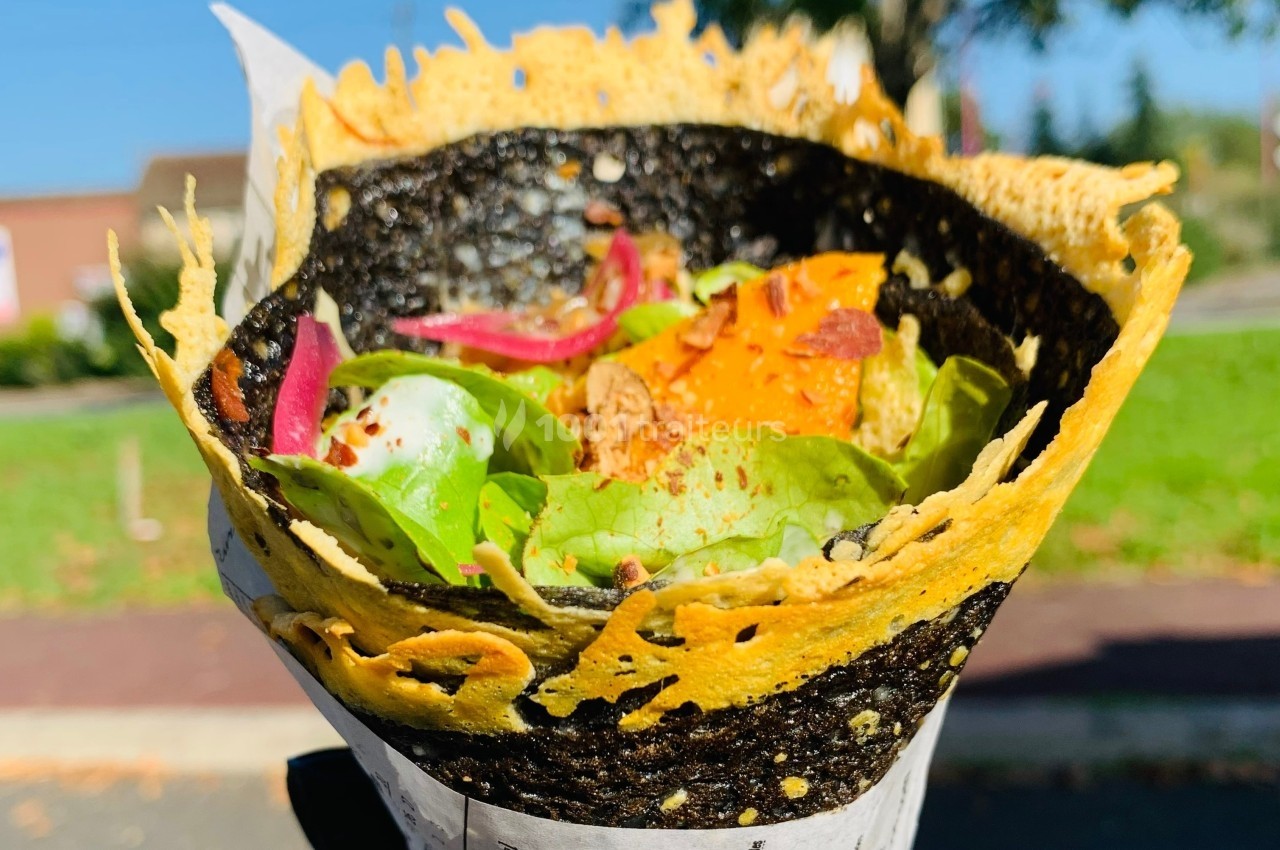 Crêpe roulée garnie de légumes frais, feuilles de salade, oignons rouges et épices, avec une enveloppe croustillante.