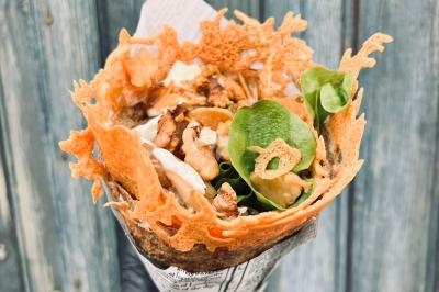 Crêpe garnie de crème fouettée, sauce caramel, éclats de noisettes et boule de praliné, tenue dans une main.