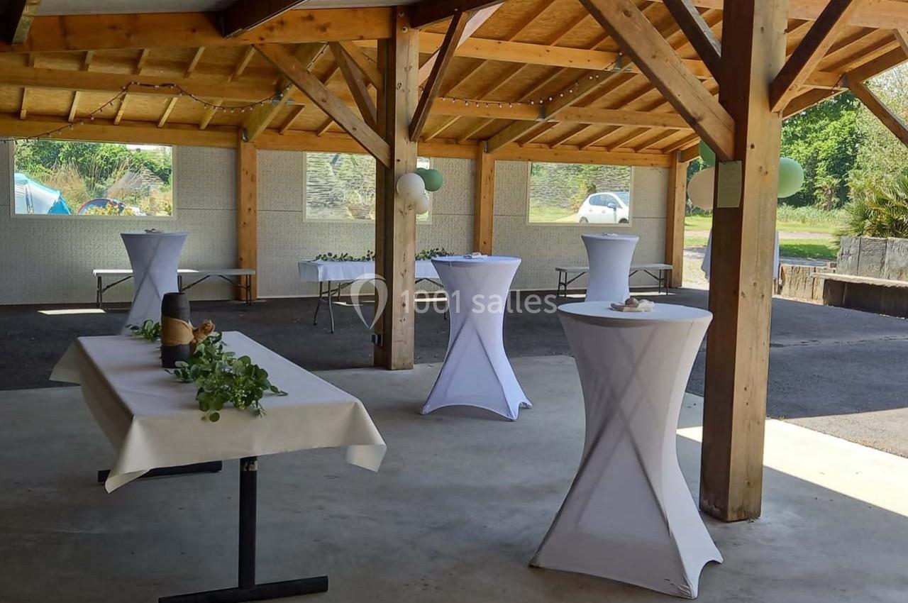 Espace couvert avec tables hautes et décorations simples, préparé pour un événement ou une réception en plein air.